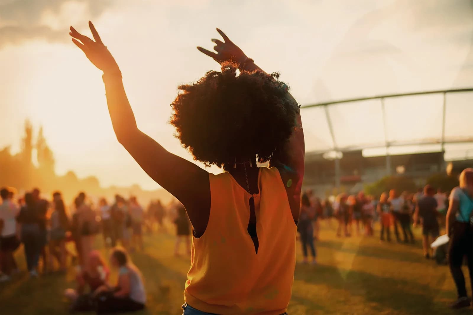 A festival-goer with arms raised in a crowd at an outdoor show at sunset