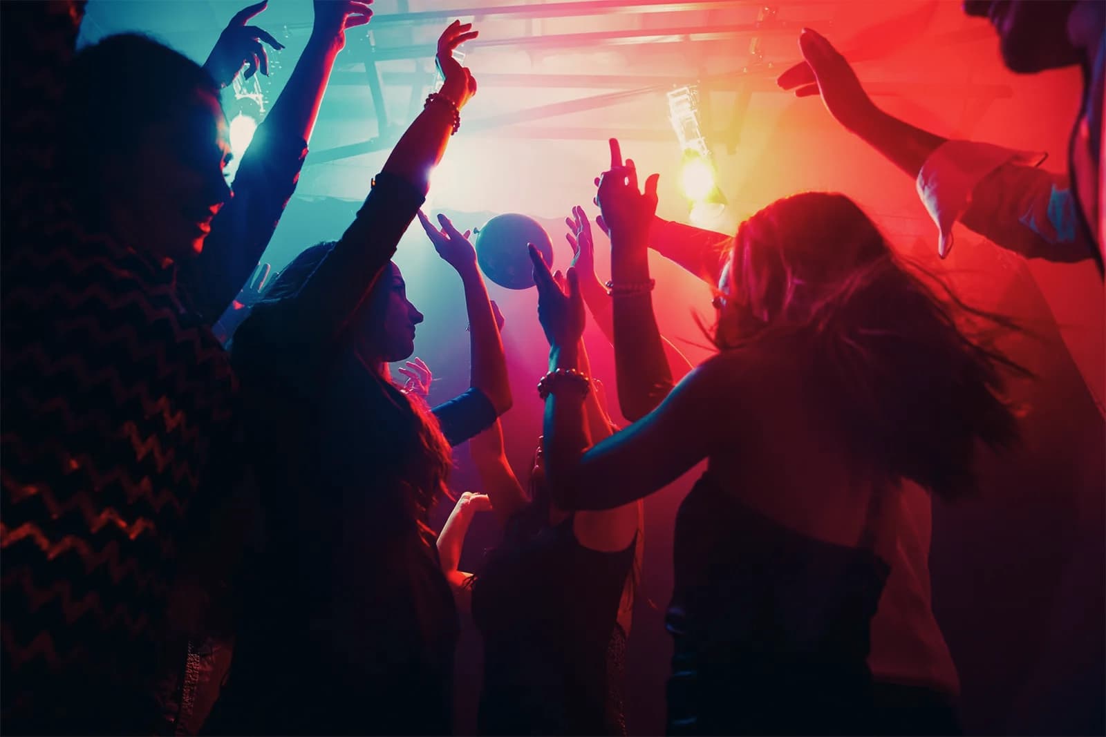 A crowd dancing with hands up under pink and blue club lights